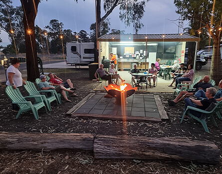 Friends and strangers sit around campfire at night enjoying company